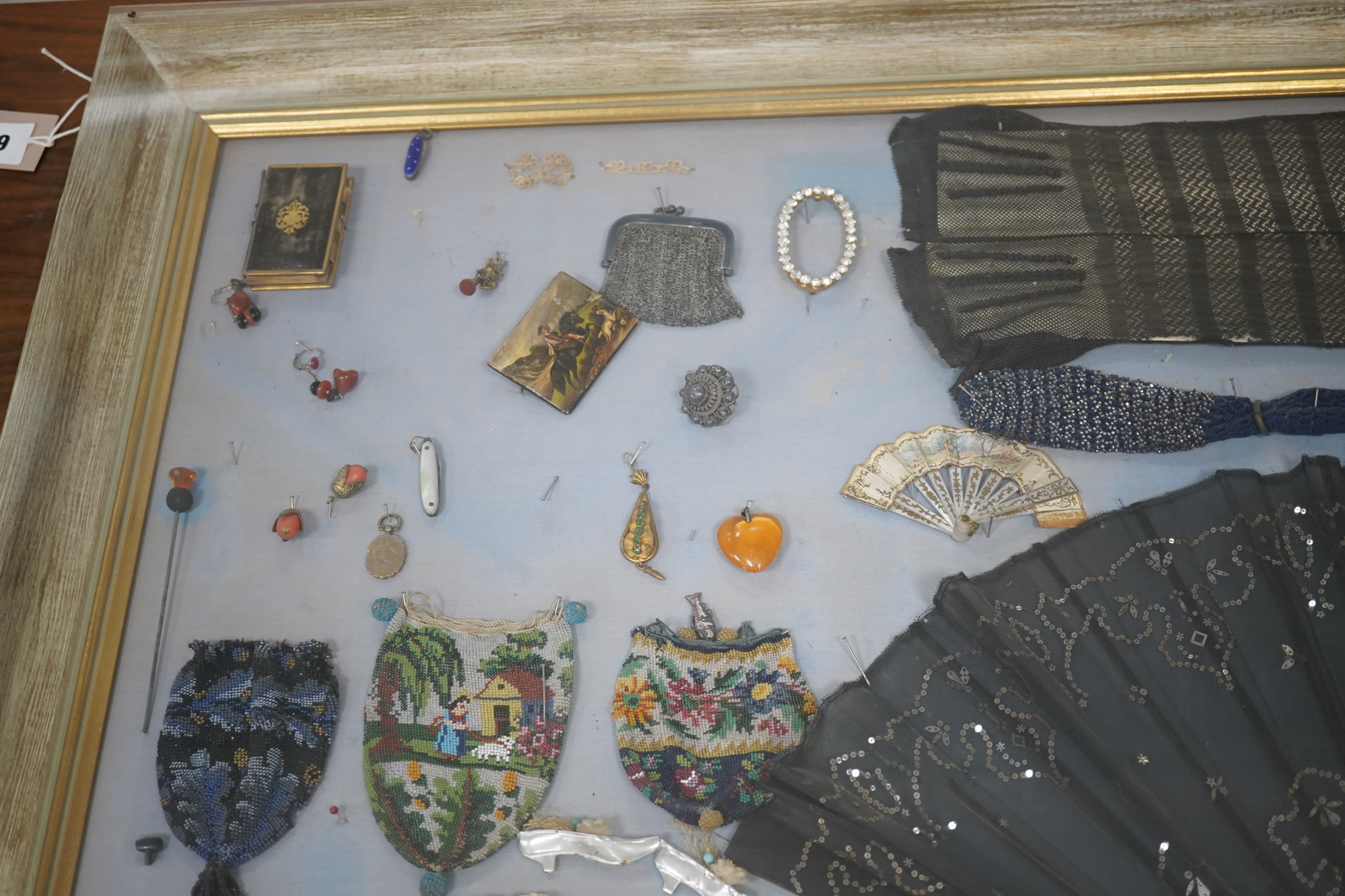 A framed display montage of late 18th and 19th century decorative ladies sequin and lace fans, beadwork reticules, cut steel misers purses, hat pins, earrings, brooches, shoe buckles and crochet mittens.100cm x 70cm. Con